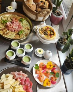 Buffet brunch gourmand Simple & Bon composé de pains maison, viennoiseries, fromages, charcuteries, saumon fumé, quiches, omelette et lard, confitures maison, pancakes, salade de fruits de saison et verrines sucrées. Présentation colorée et conviviale sur table.