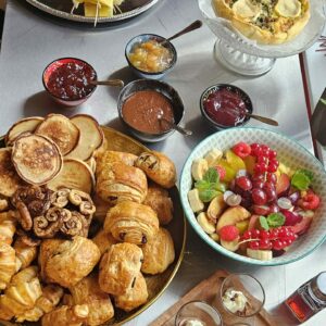 Buffet brunch gourmand Simple & Bon composé de pains maison, viennoiseries, fromages, charcuteries, saumon fumé, quiches, omelette et lard, confitures maison, pancakes, salade de fruits de saison et verrines sucrées. Présentation colorée et conviviale sur table.