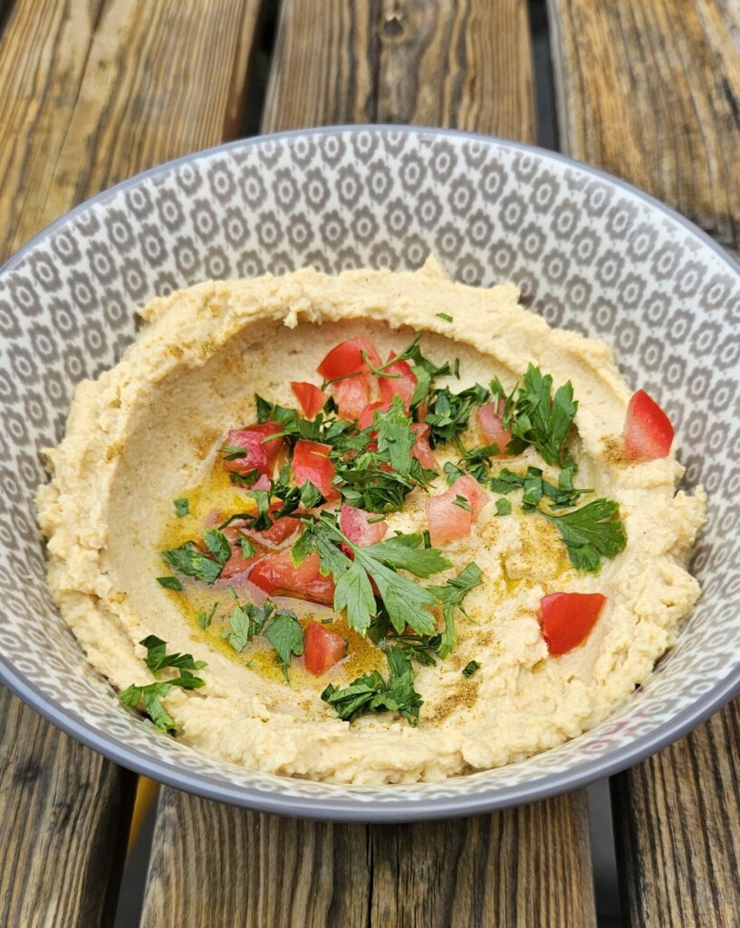 Bol de houmous libanais crémeux garni d’huile d’olive, de persil frais et de tomates.
