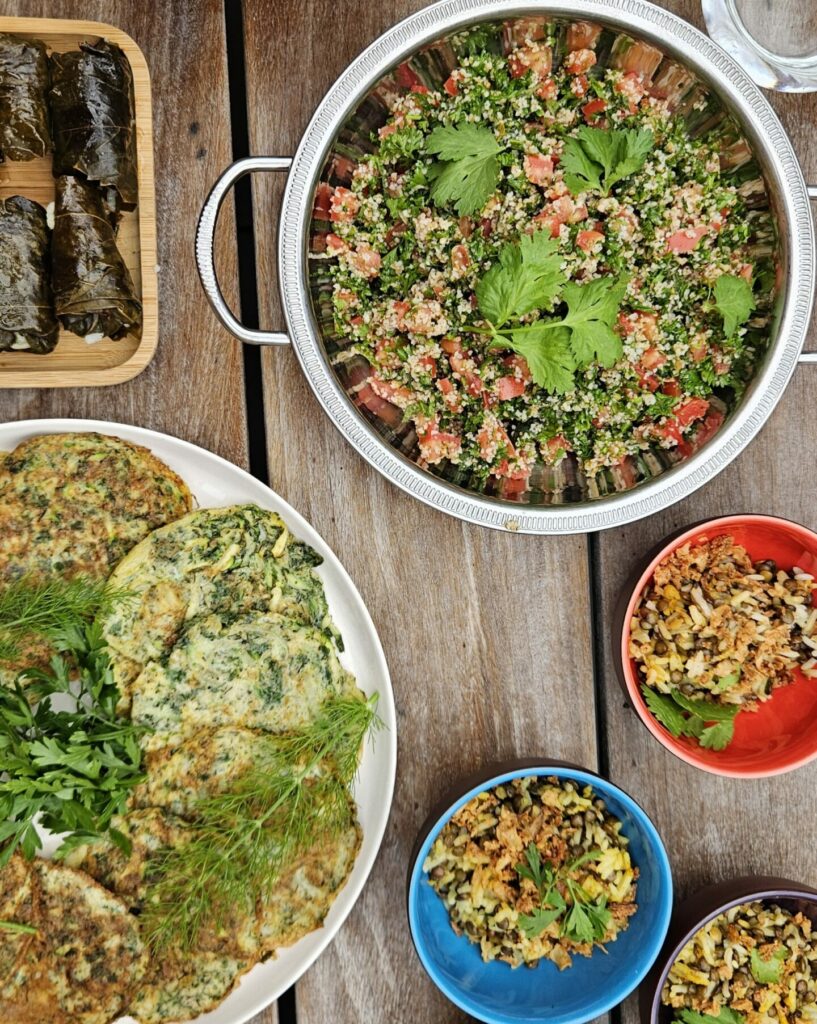 Assortiment de mezzés libanais comprenant taboulé, houmous, feuilles de vigne farcies, omelettes aux herbes et riz aux lentilles.