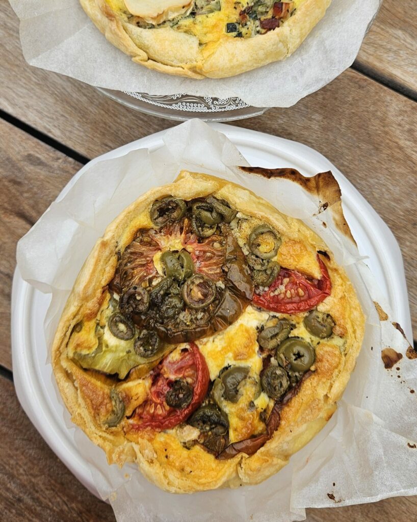 Deux tartes salées maison aux légumes frais, l’une garnie de fromage de chèvre et l’autre de tomates et olives, sur table en bois
