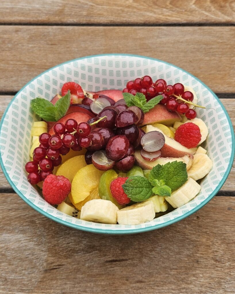 Bol de salade de fruits frais colorés avec banane, raisin, framboises, groseilles, nectarine et feuilles de menthe.