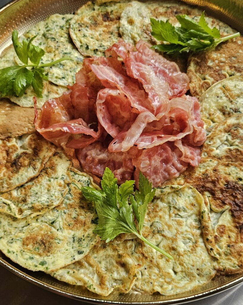 Plateau doré garni d’omelettes aux herbes accompagnées de bacon croustillant et décoré de persil frais.