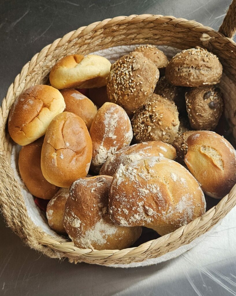 Corbeille en osier garnie de petits pains blancs et aux graines, présentés pour un buffet ou un repas traiteur.