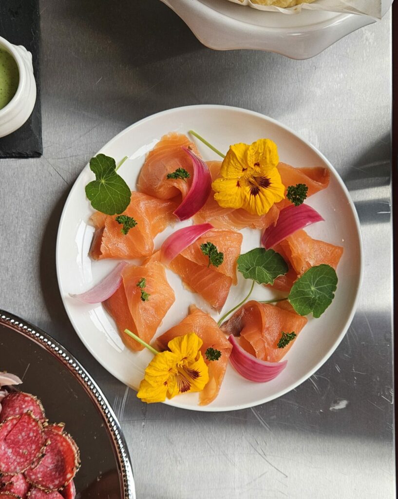 Assiette de saumon fumé décorée de pickles d’oignon rouge, herbes fraîches et fleurs comestibles.
