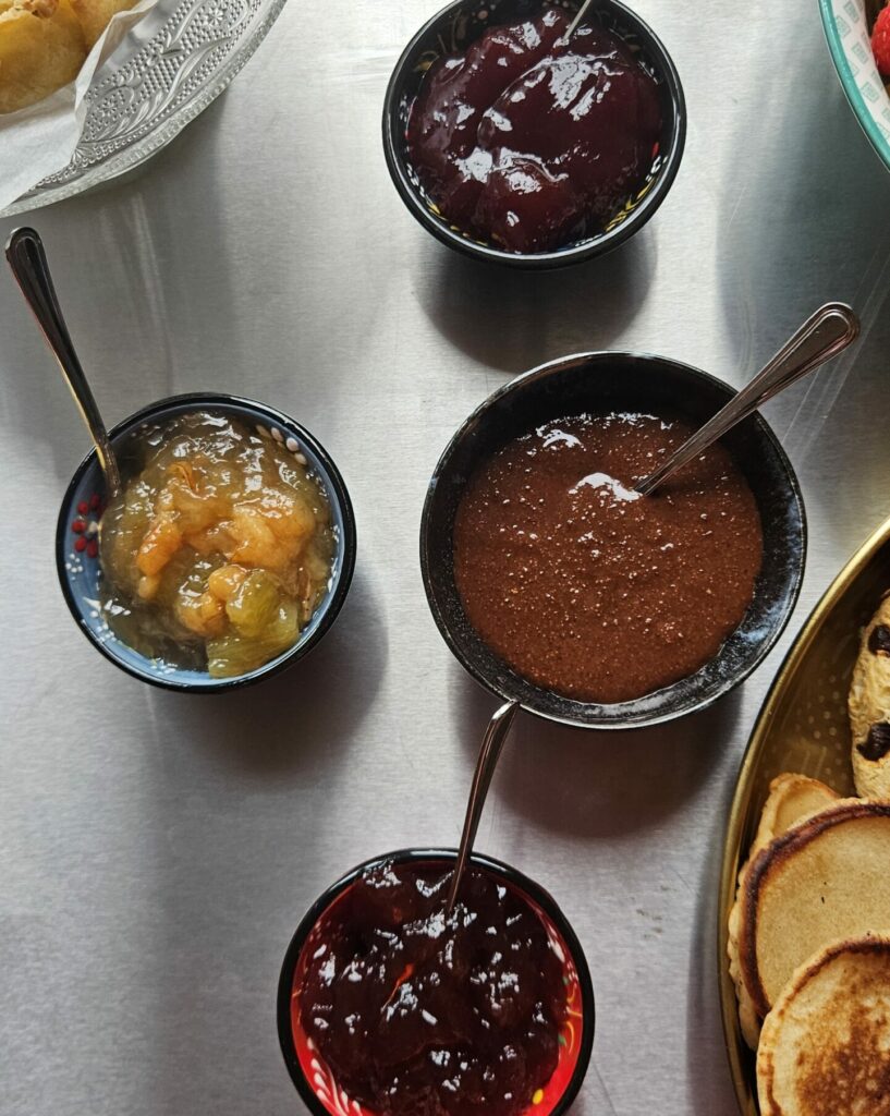 Assortiment de trois confitures maison et d’une pâte à tartiner au cacao, présentés dans des petits bols colorés.