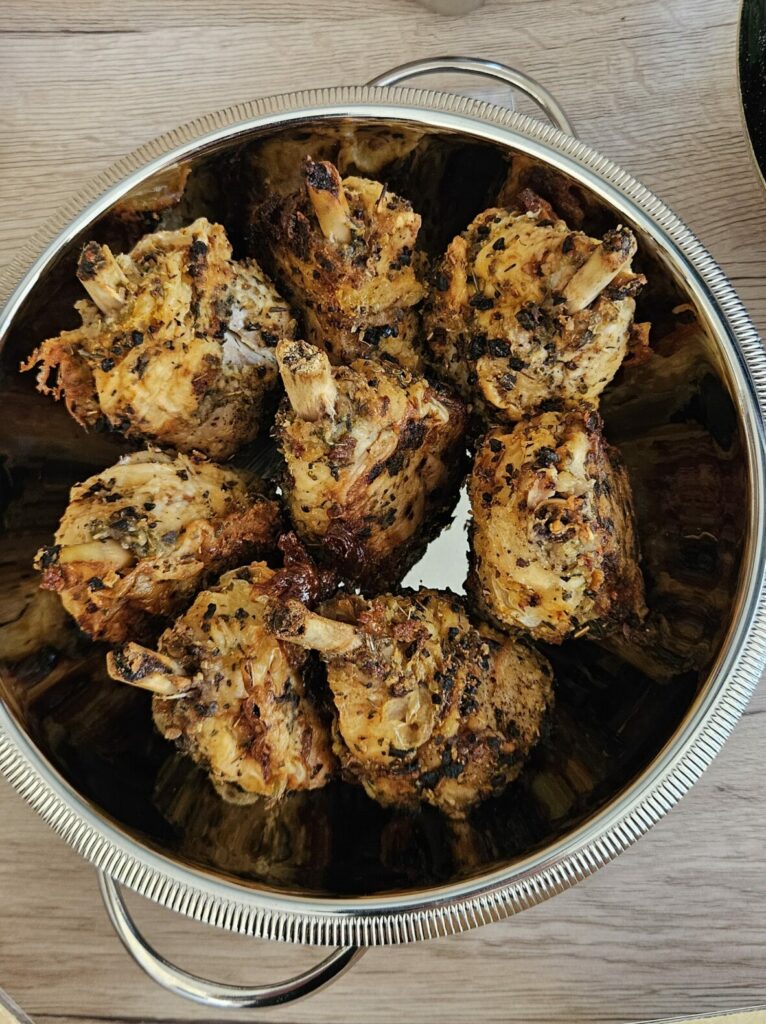 Plat en inox rempli de pilons de poulet marinés et grillés aux herbes, présentés pour un buffet.