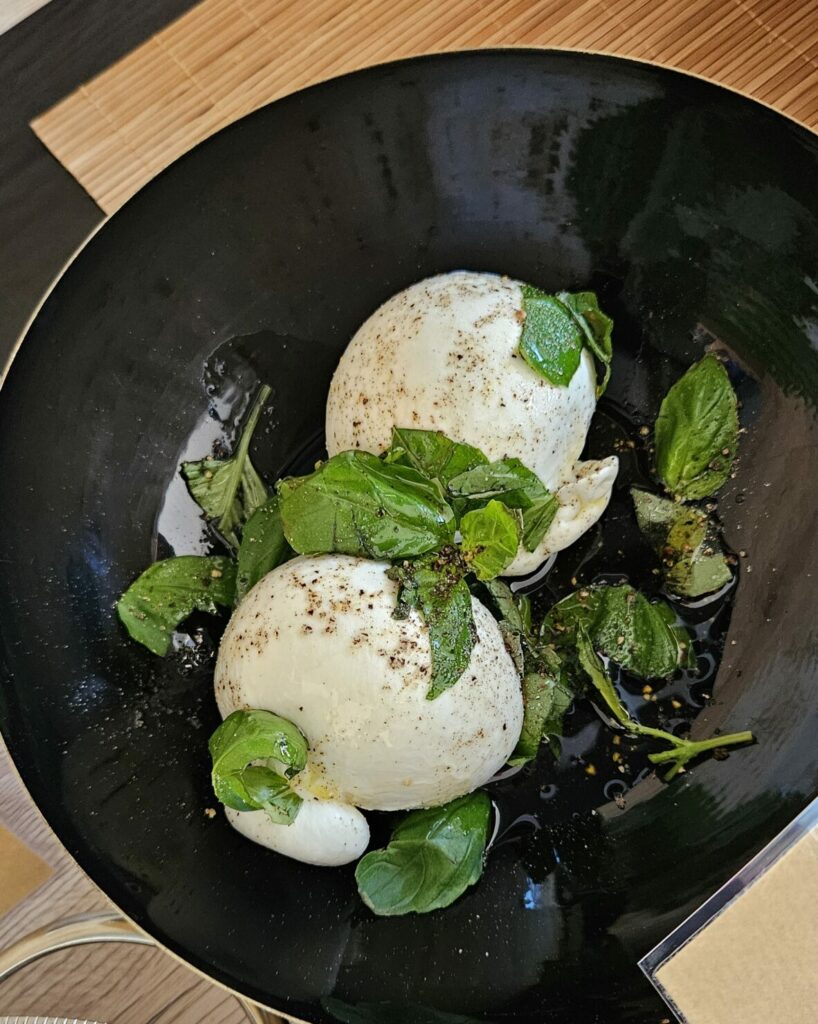 Assiette de burrata crémeuse assaisonnée d’huile d’olive, de basilic frais et de poivre noir