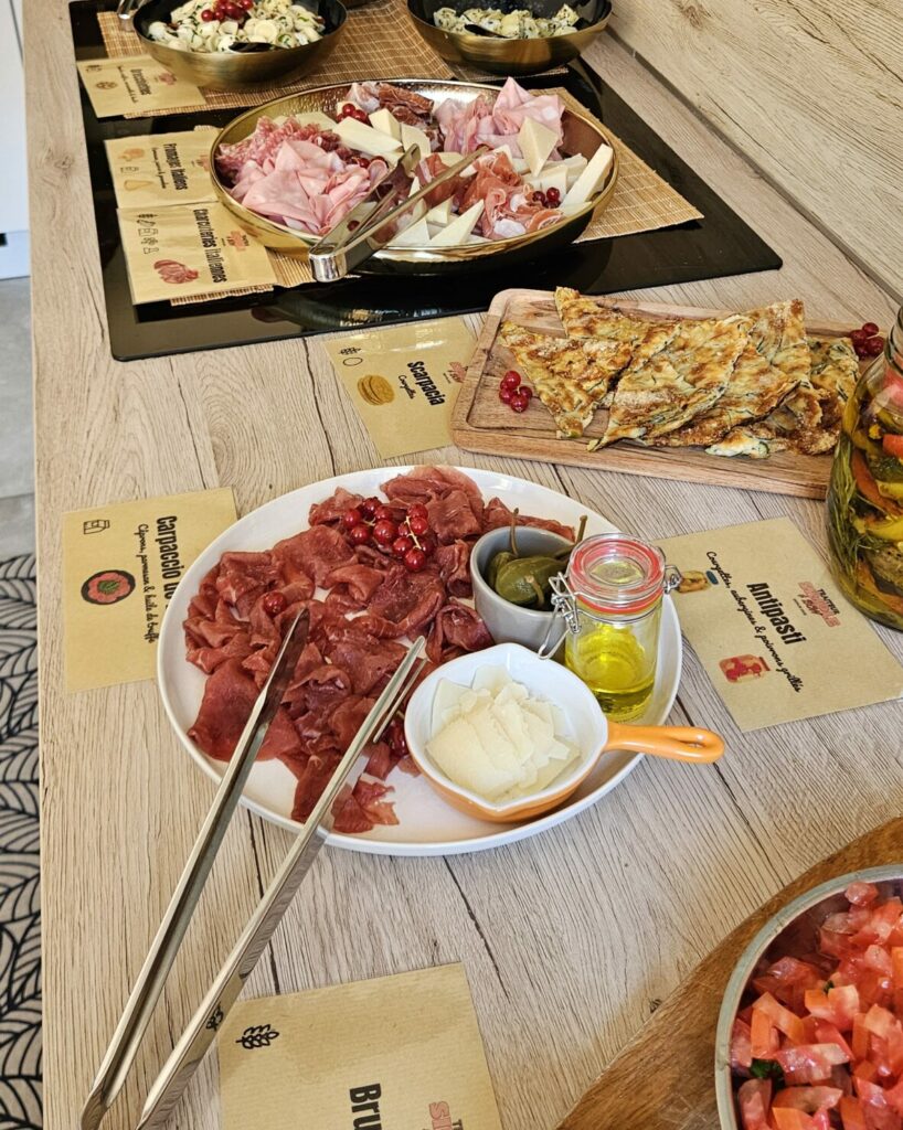 Buffet italien complet avec antipasti, bruschetta, carpaccio, scarpaccia aux courgettes, charcuteries, fromages italiens, arancini, burrata et légumes grillés.