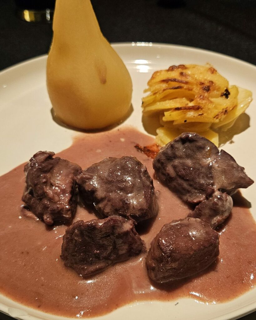 Assiette de marcassin mijoté au vin rouge, servi avec une poire pochée et un gratin doré de pommes de terre.