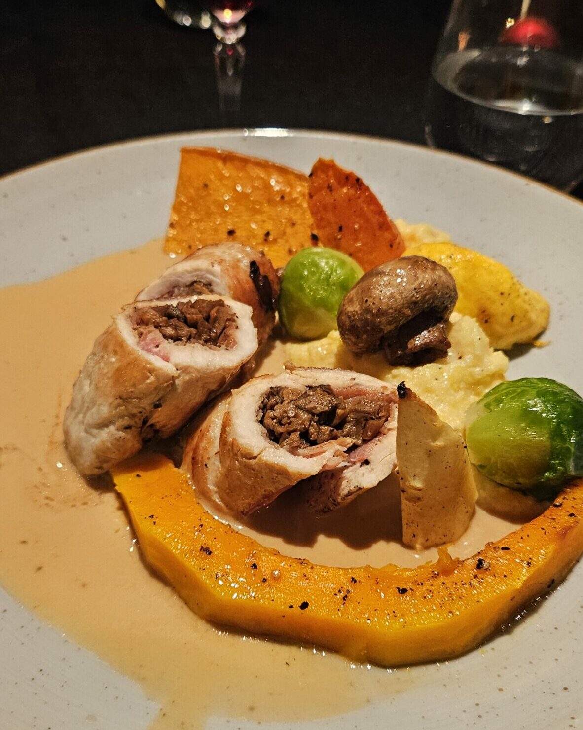 Roulade de dinde farcie aux cèpes, servie avec polenta crémeuse, légumes rôtis et sauce brune sur assiette festive.