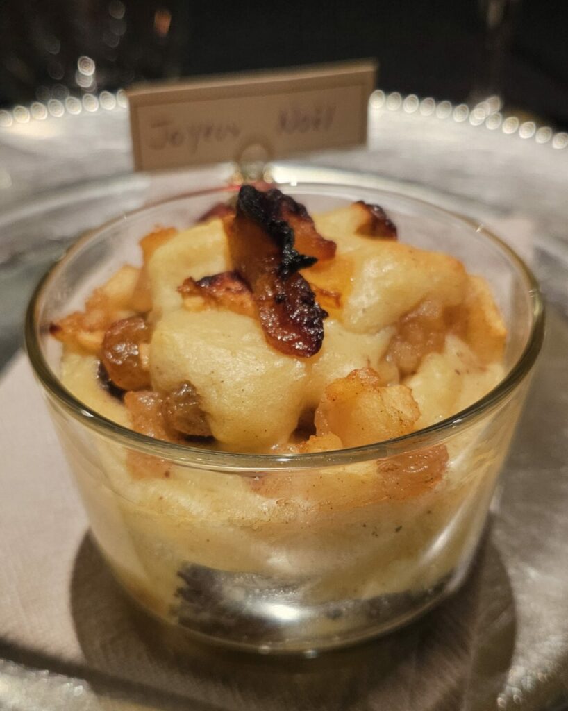 Verrine de tiramisu salé au boudin noir et pommes caramélisées, servie chaude dans un ramequin en verre sur une table de fête.