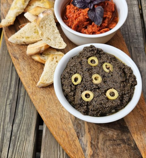 planche apéritive avec trois tartinades : tapenade noire, pesto de poivrons rouges, houmous d’olives vertes, accompagnées de pain grillé